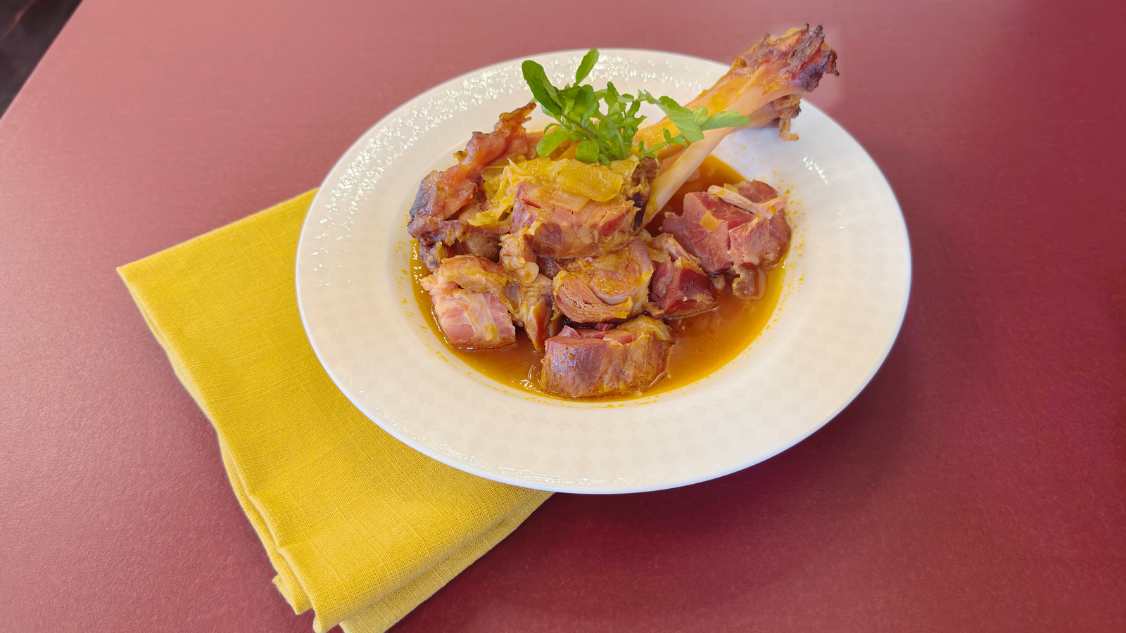 骨付きアイスバインと食べやすく切った肉を白い皿に盛り付けたミネストローネ
